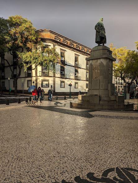 Golden sunlight breaks through the grey clouds to light up the statue of Zarco in the middle of Funchal
